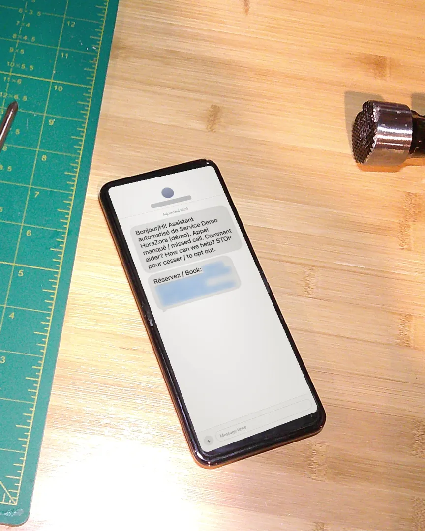 A phone on a workbench showing the automatic text from the HoraZora demo after a missed call, with a booking link.